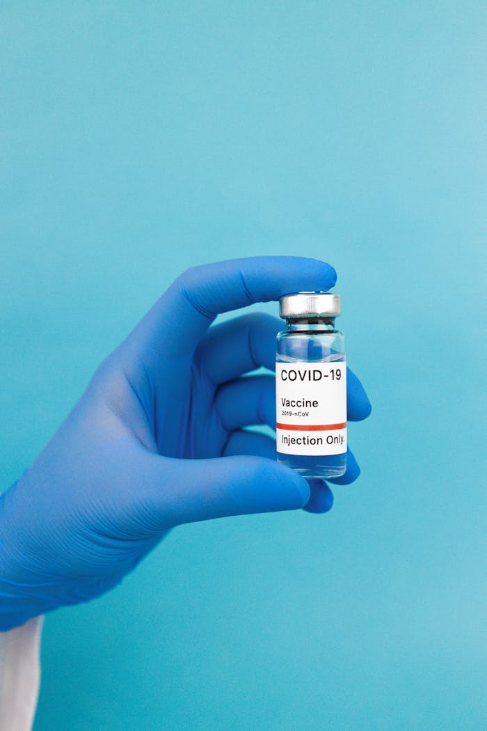 Close-up of a gloved hand holding a COVID-19 vaccine vial against a blue background.