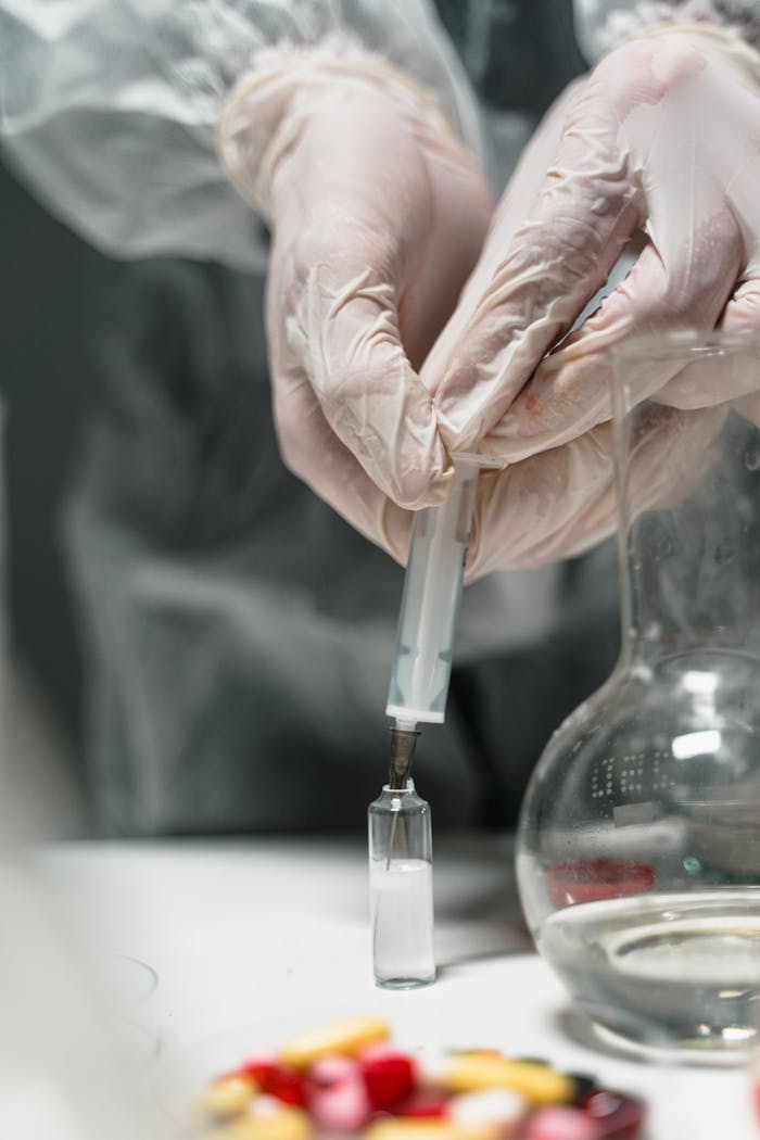 Scientist uses syringe to inject liquid into vial, showcasing laboratory work.